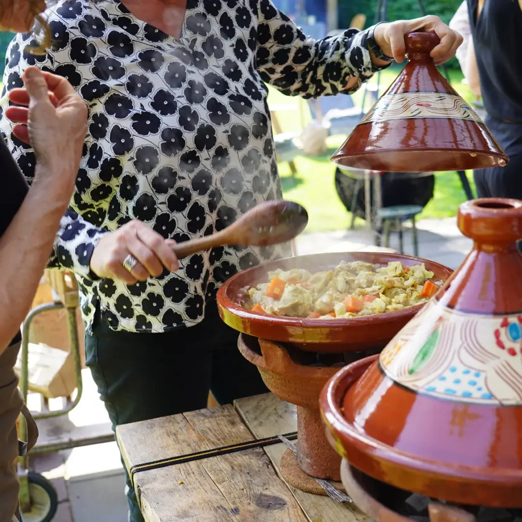 Groep bereidt gerechten in de buitenlucht met behulp van driepoten en tajines.